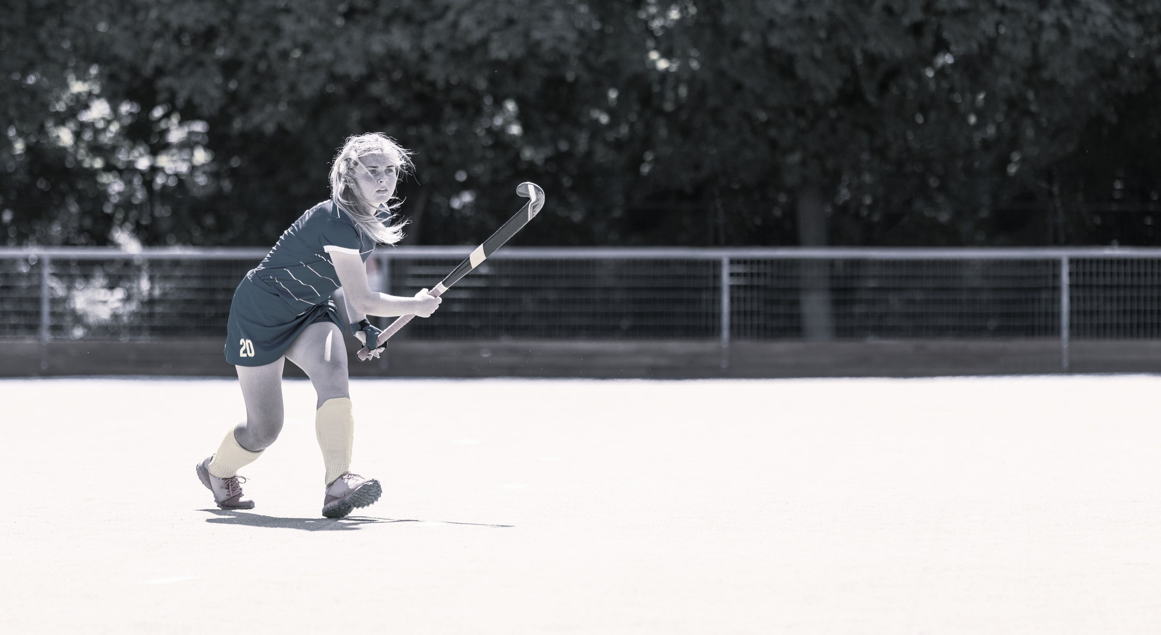Una jugadora de hockey sobre césped, palo en alto, a punto de pegarle a la bocha durante un partido.